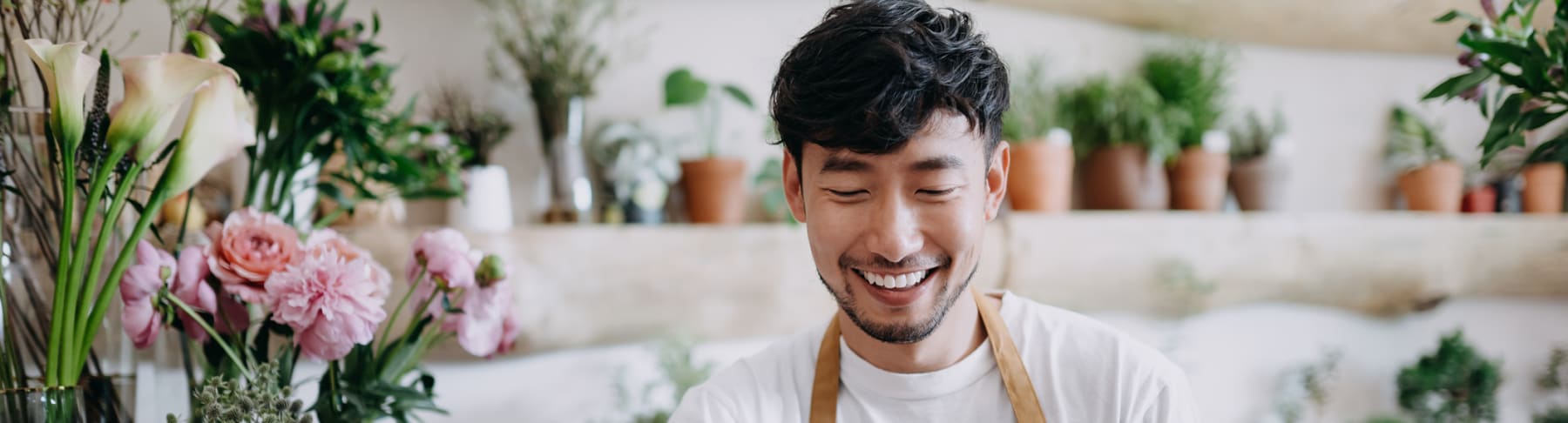 Asian male florist uses tablet in shop.