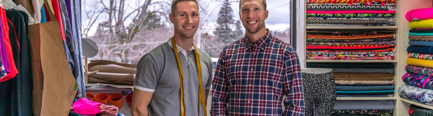 Two men pose in clothing workshop.