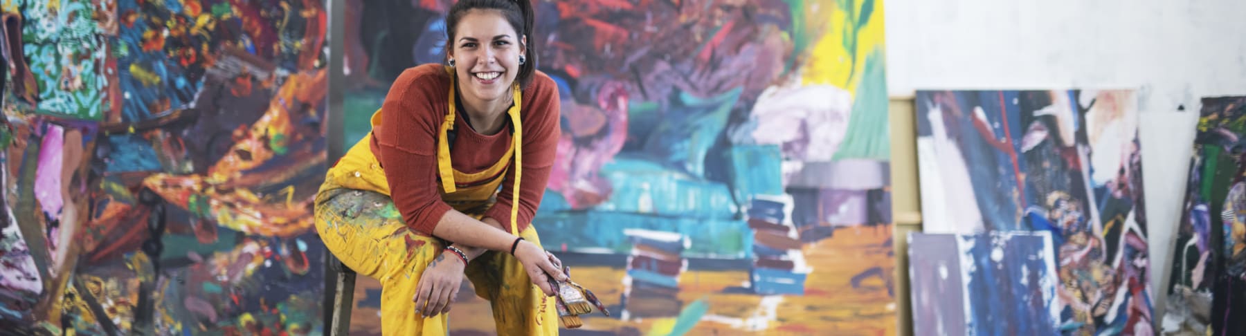 Hispanic artist poses in front of paintings.