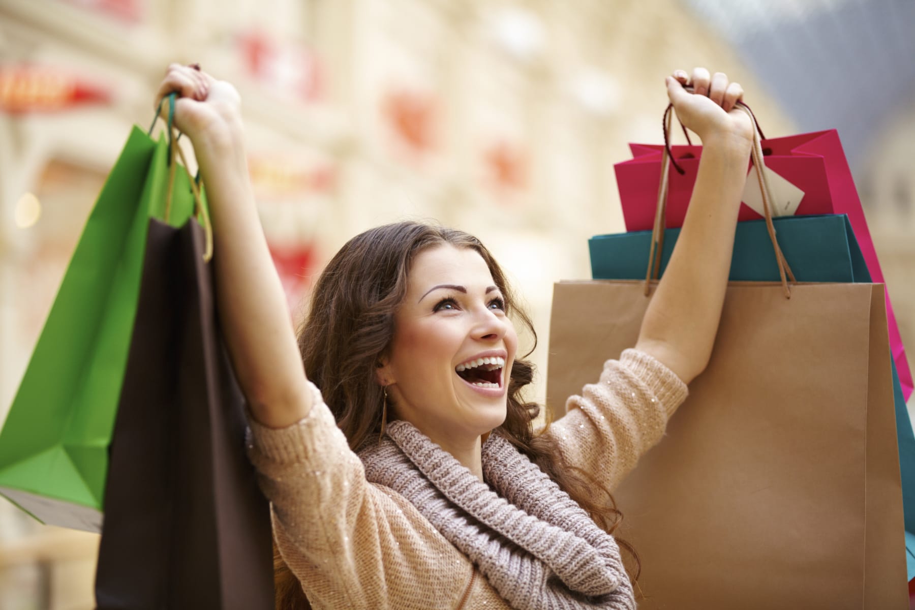 Woman excitedly raises arms full of shopping bags.