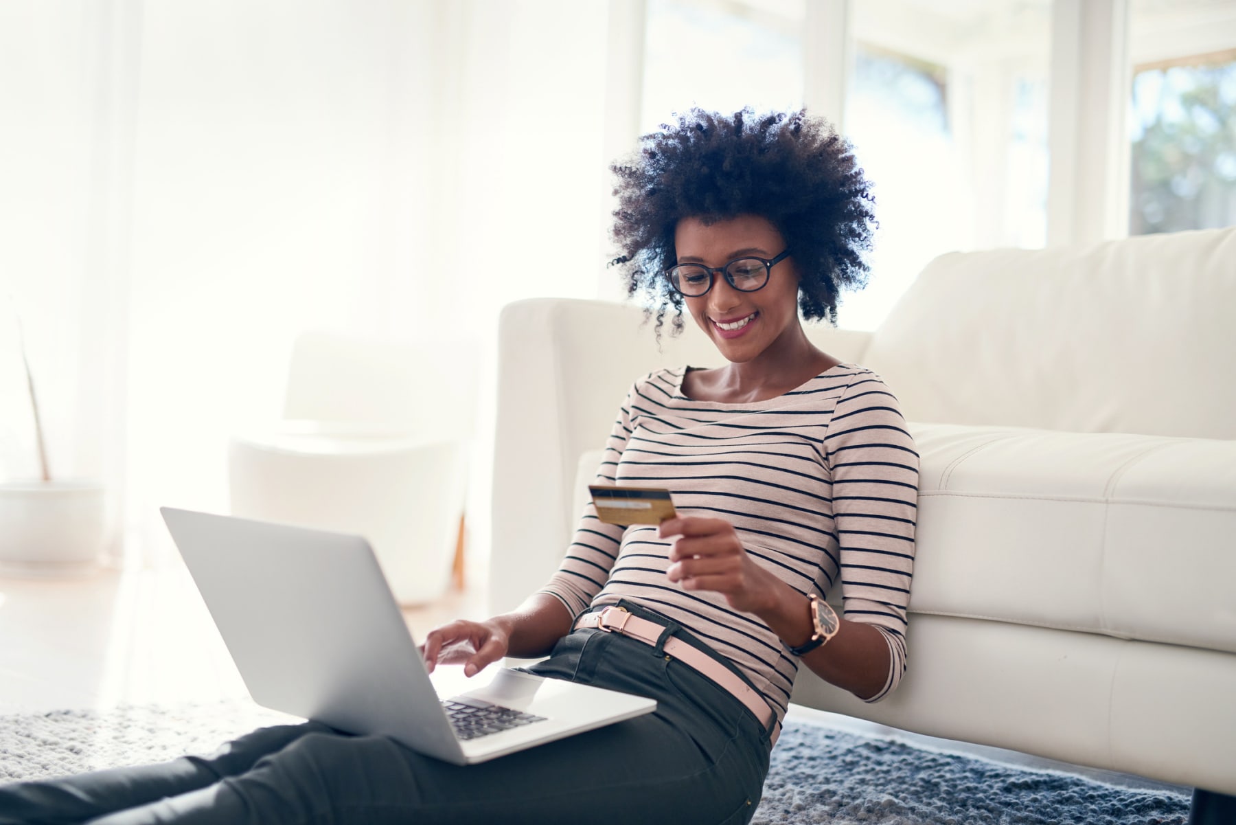 Young woman holds credit card while using laptop.