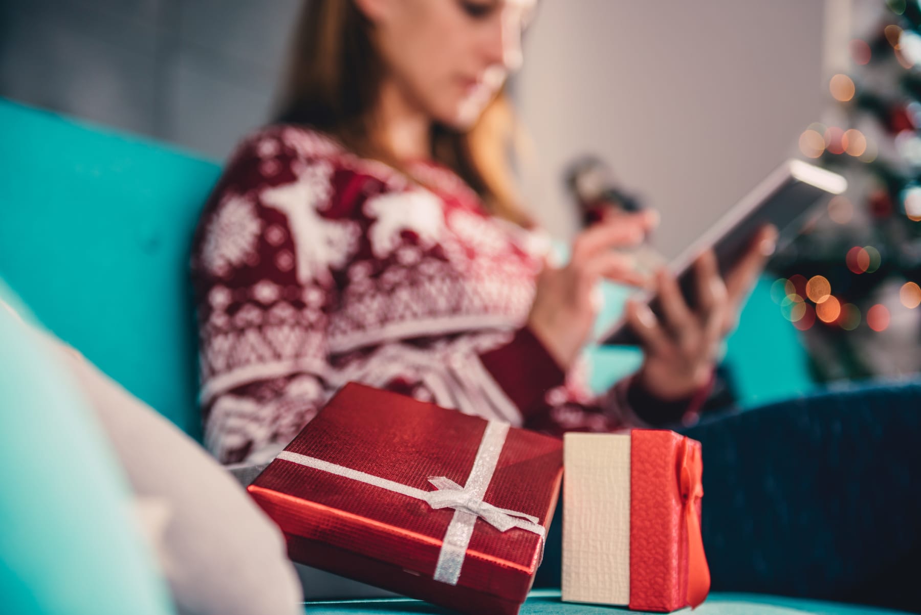 Woman shopping online next to holiday gifts.