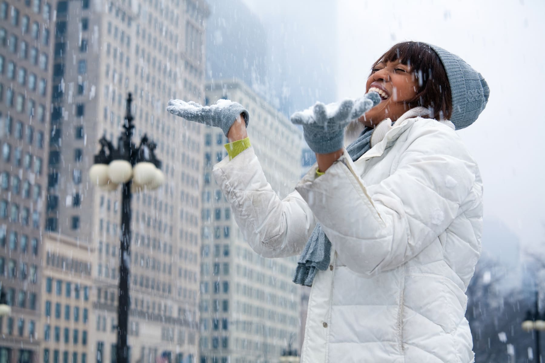 Woman laughs while catching snow in the city.
