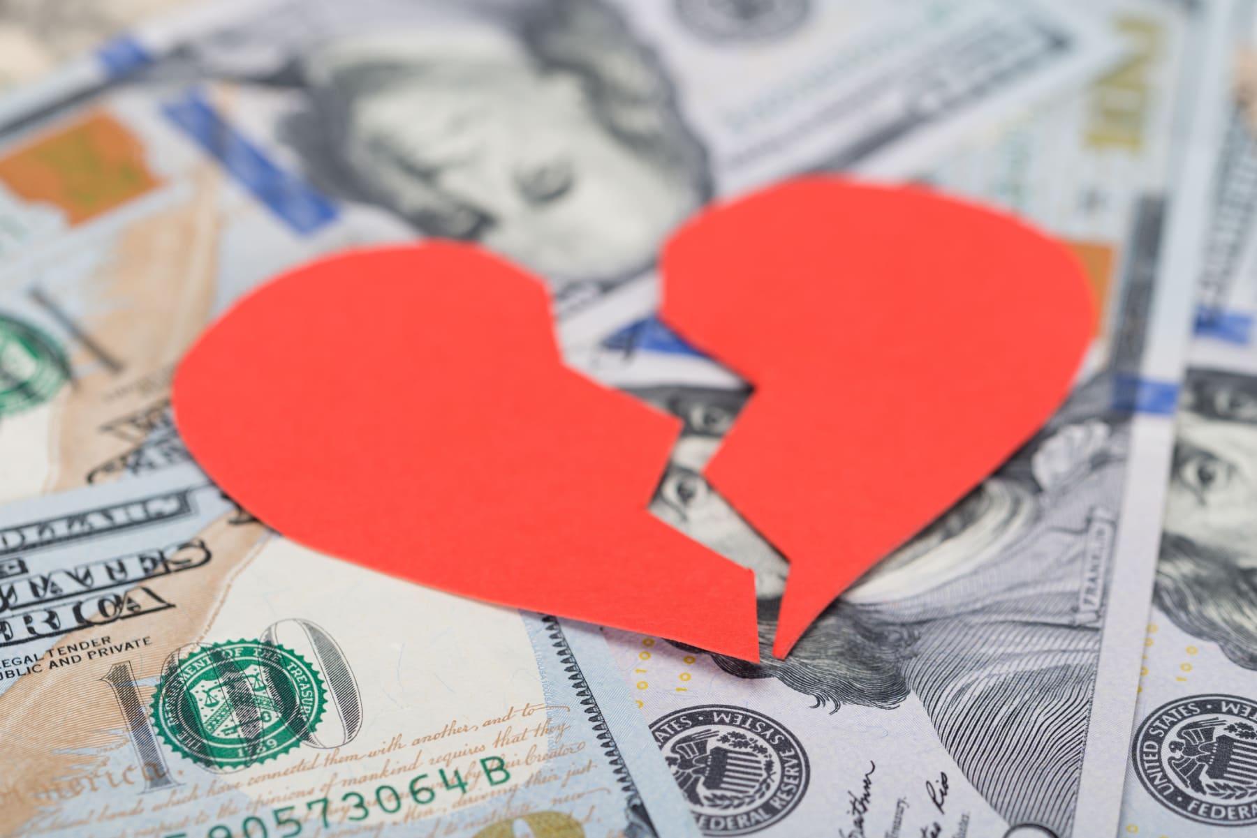 Paper broken heart sits on top of hundred-dollar bills.