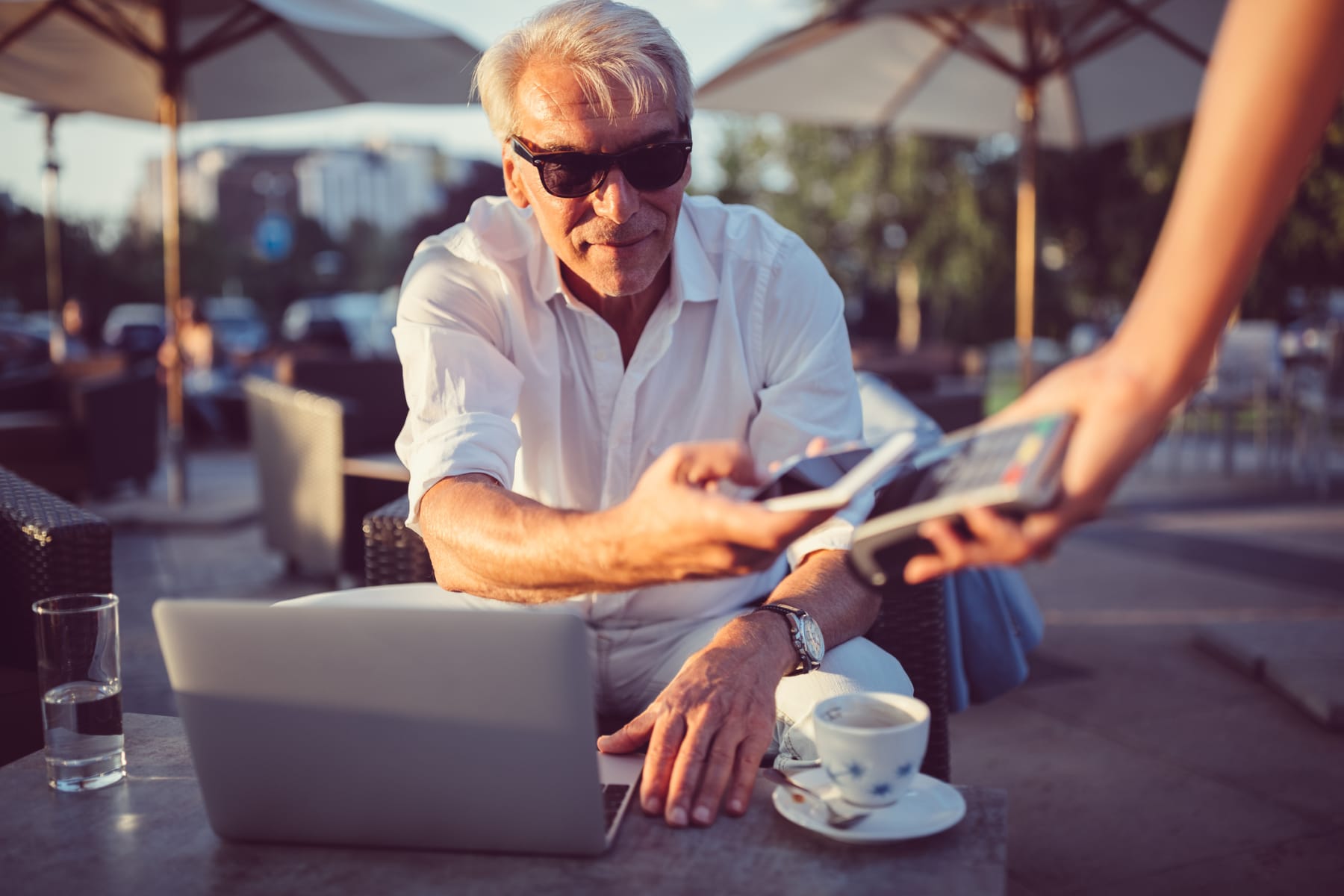Seated outdoors, an older man in sunglasses makes a mobile payment.