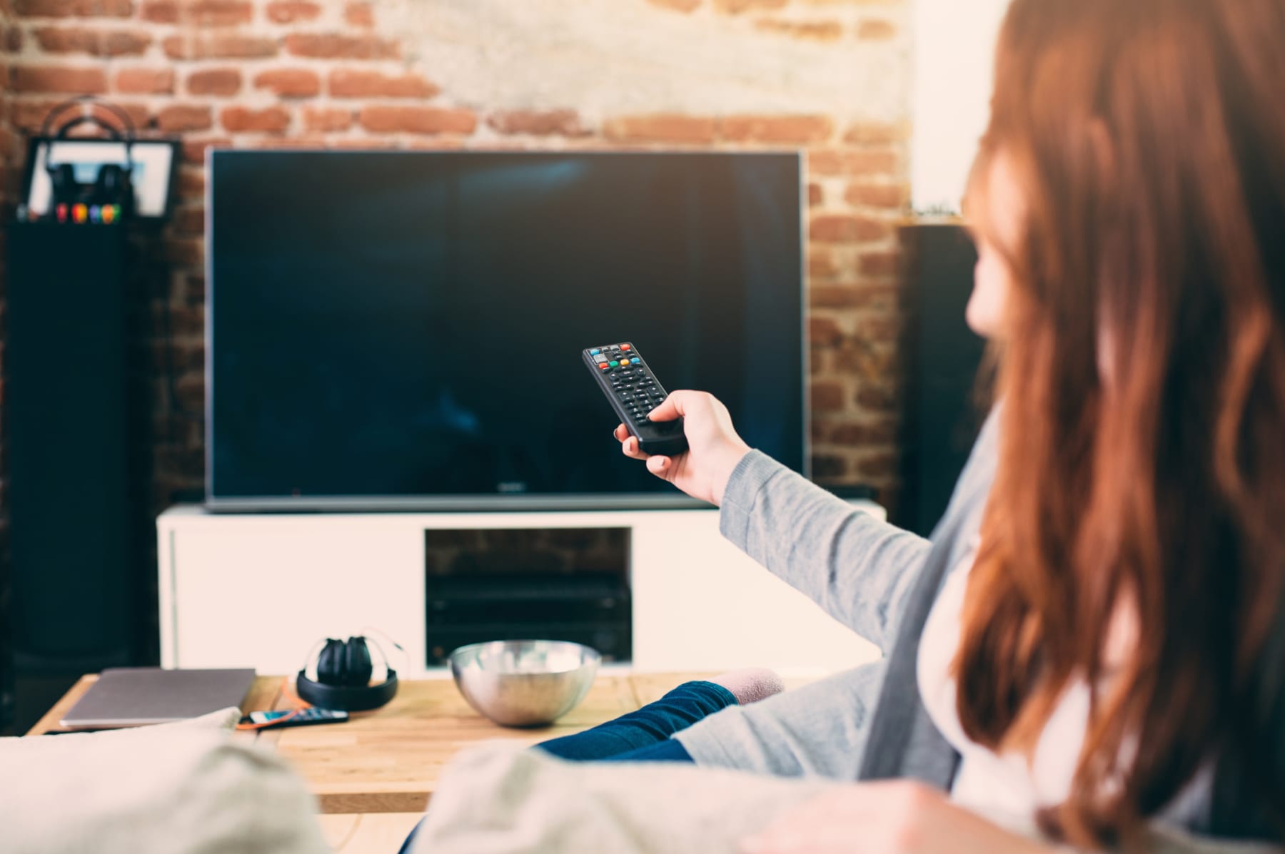 Woman turns on flat-screen TV using remote.