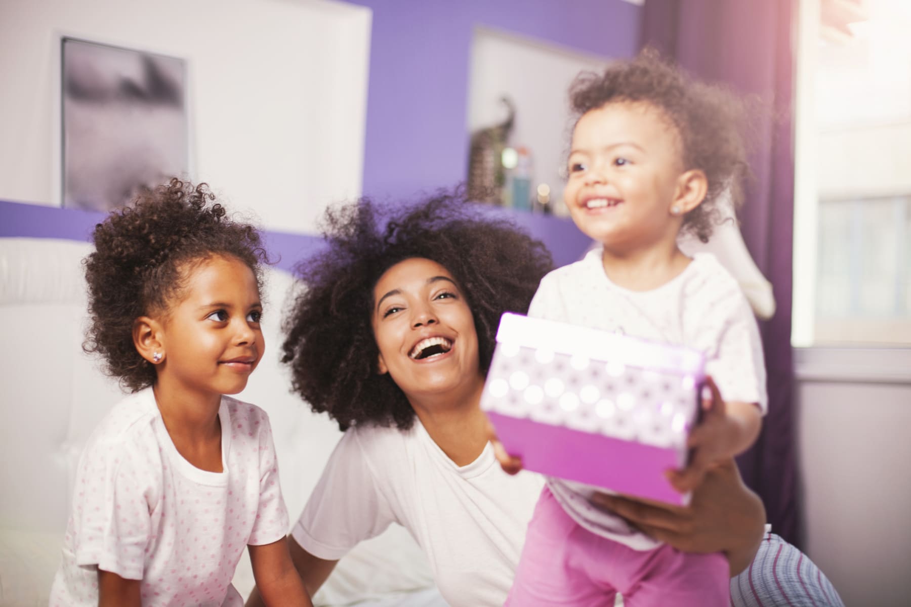 Two young kids give gift to mom on bed.