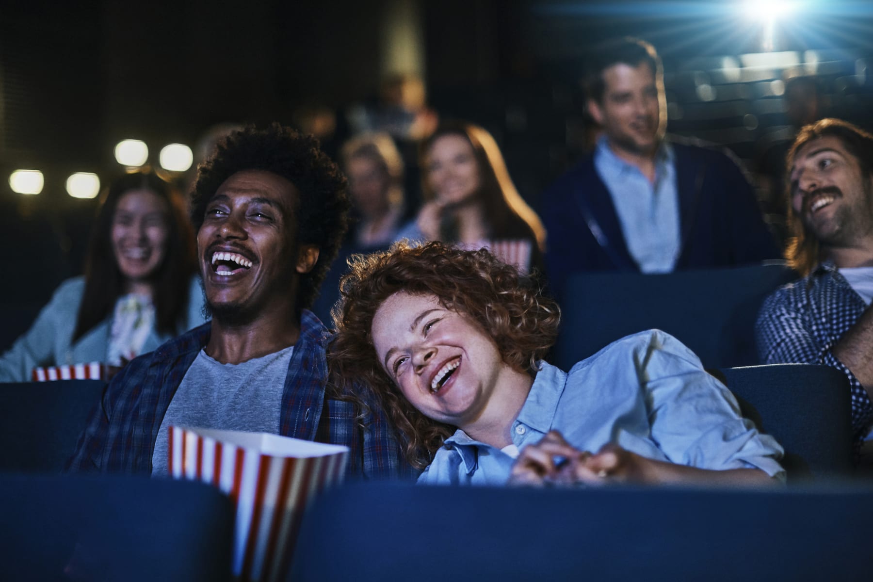Friends laugh while watching movie in theater.