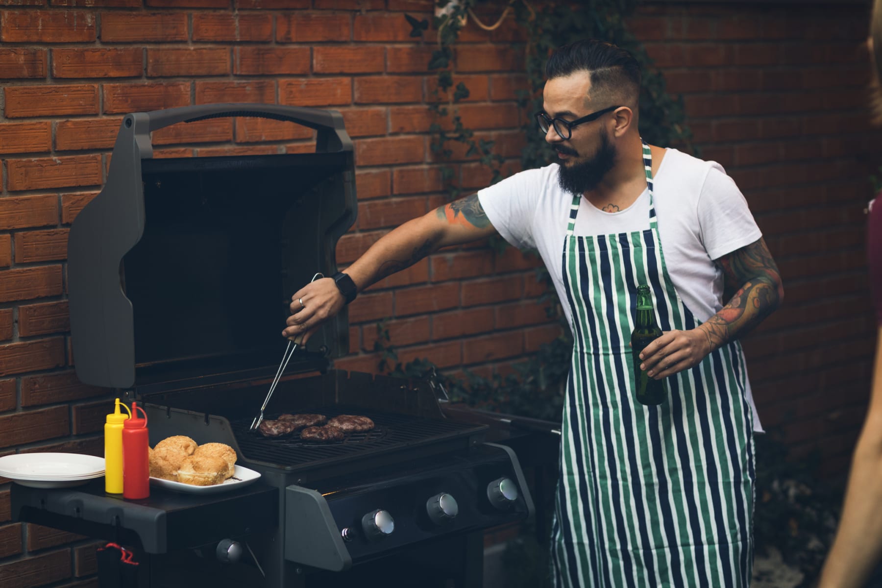 A man cooks burgers on an outdoor grill.