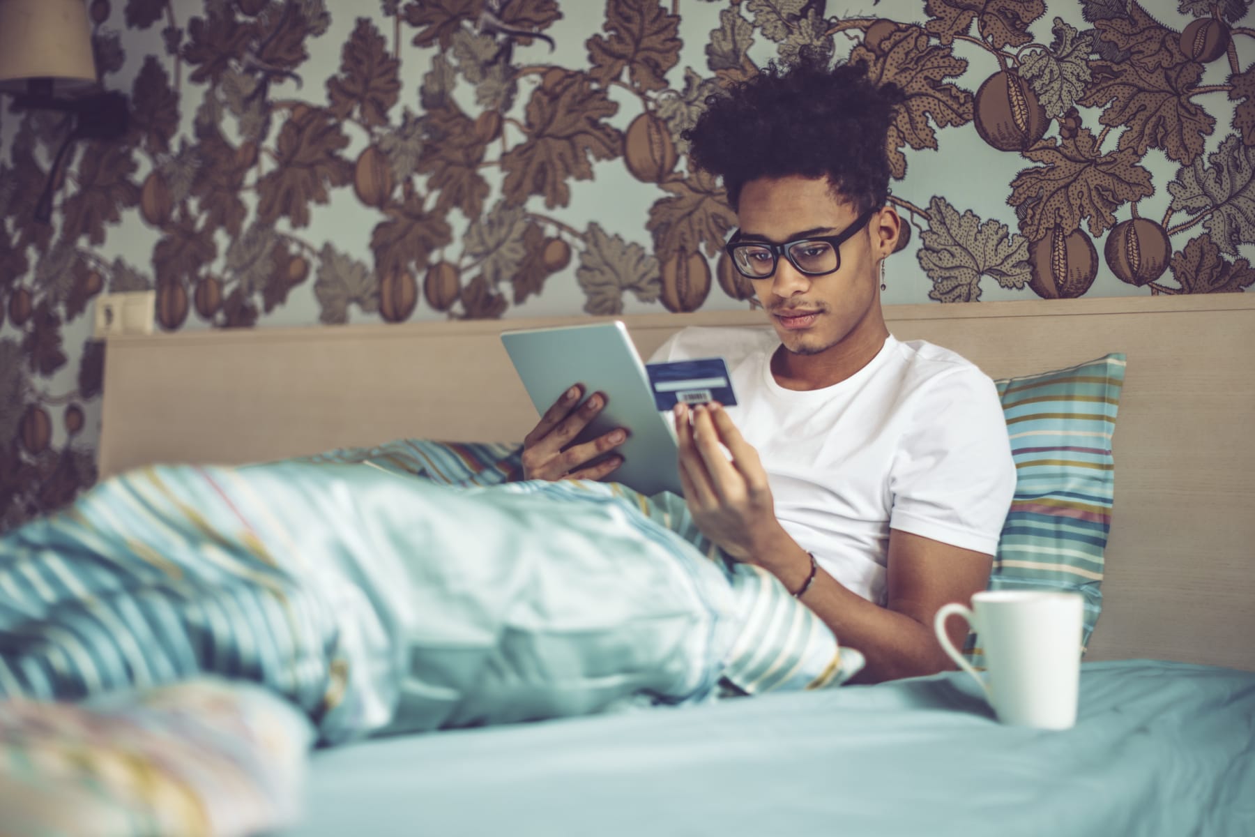 Young man shops online while lying in bed.