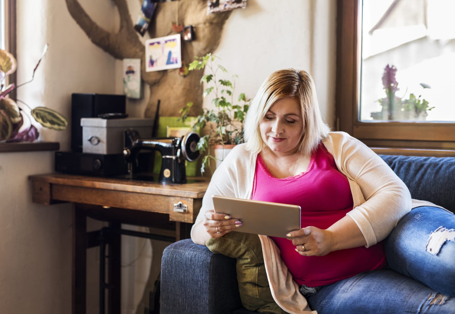 Woman looks at tablet while sitting on couch.