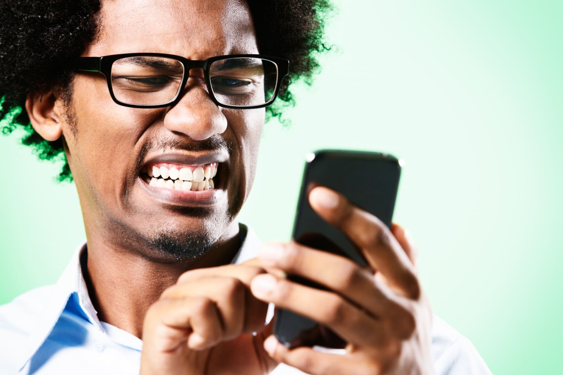 Young man grimaces at cell phone.