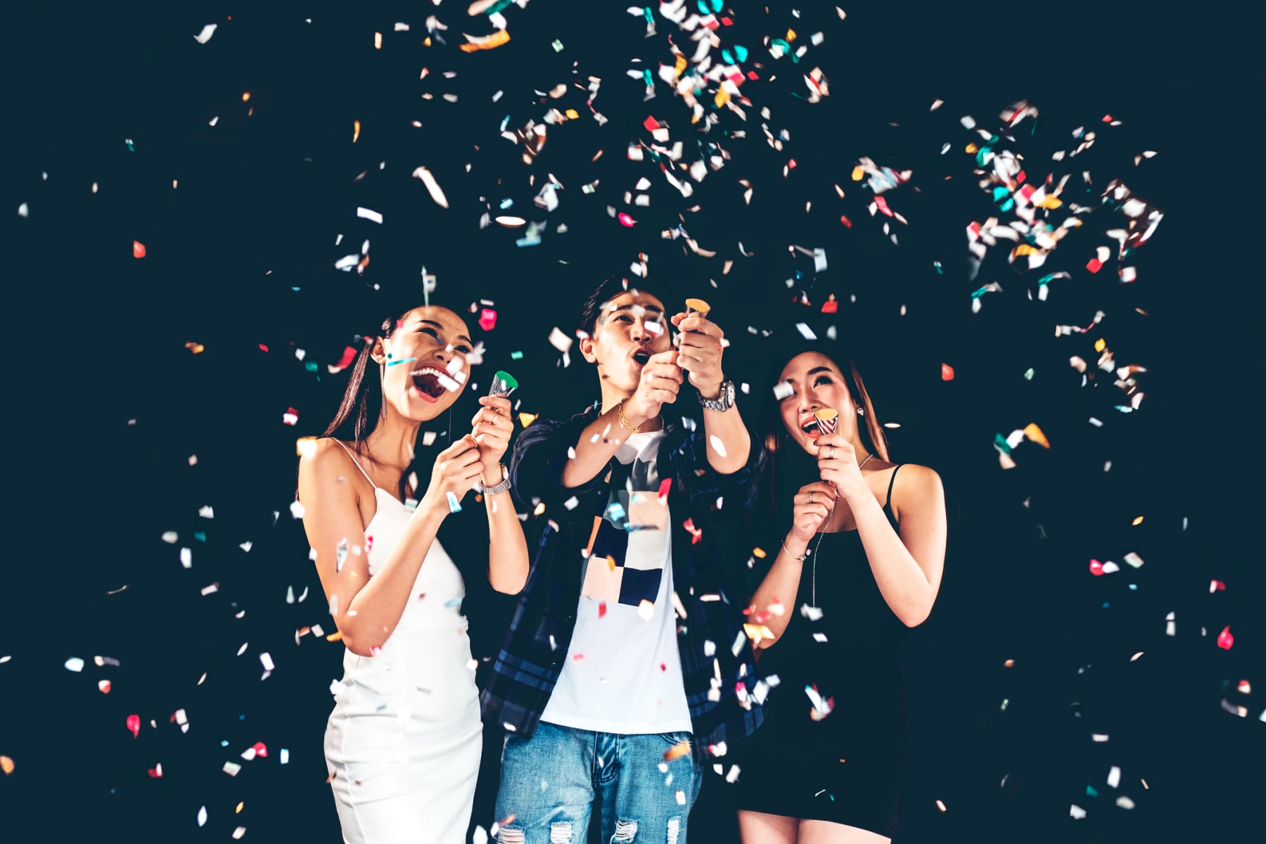 Three young people stand under confetti and celebrate.