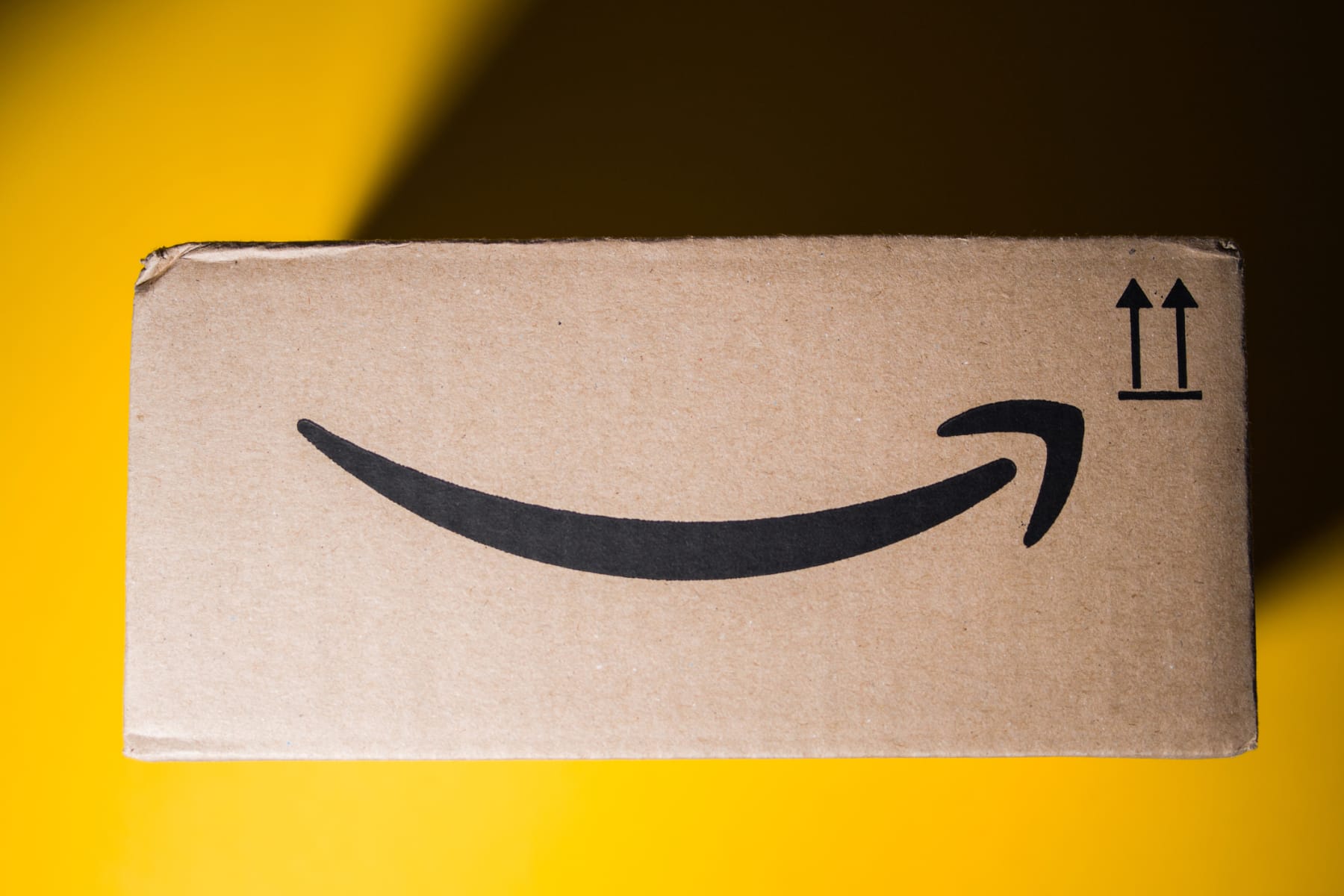 An Amazon box, with the smile arrow logo facing outward, in front of a yellow background.