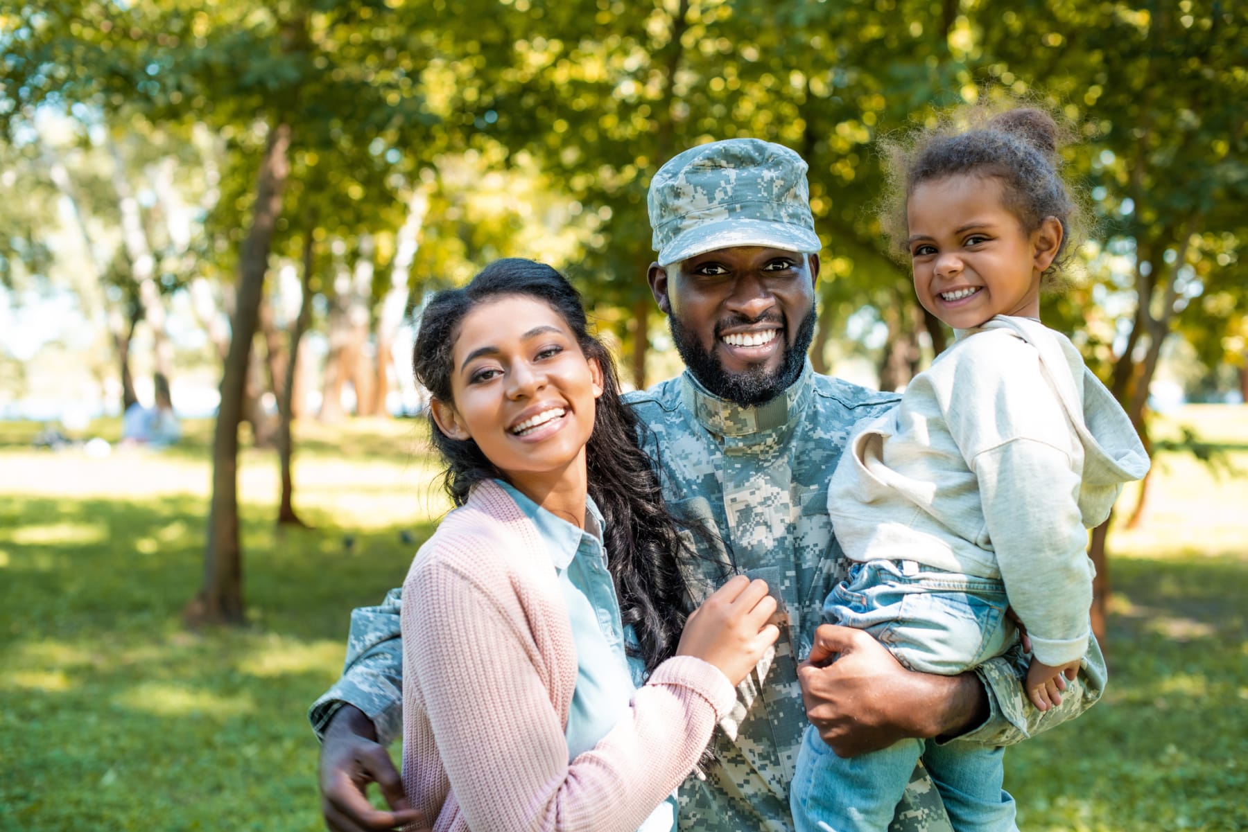A happy military member poses with his family in a park.