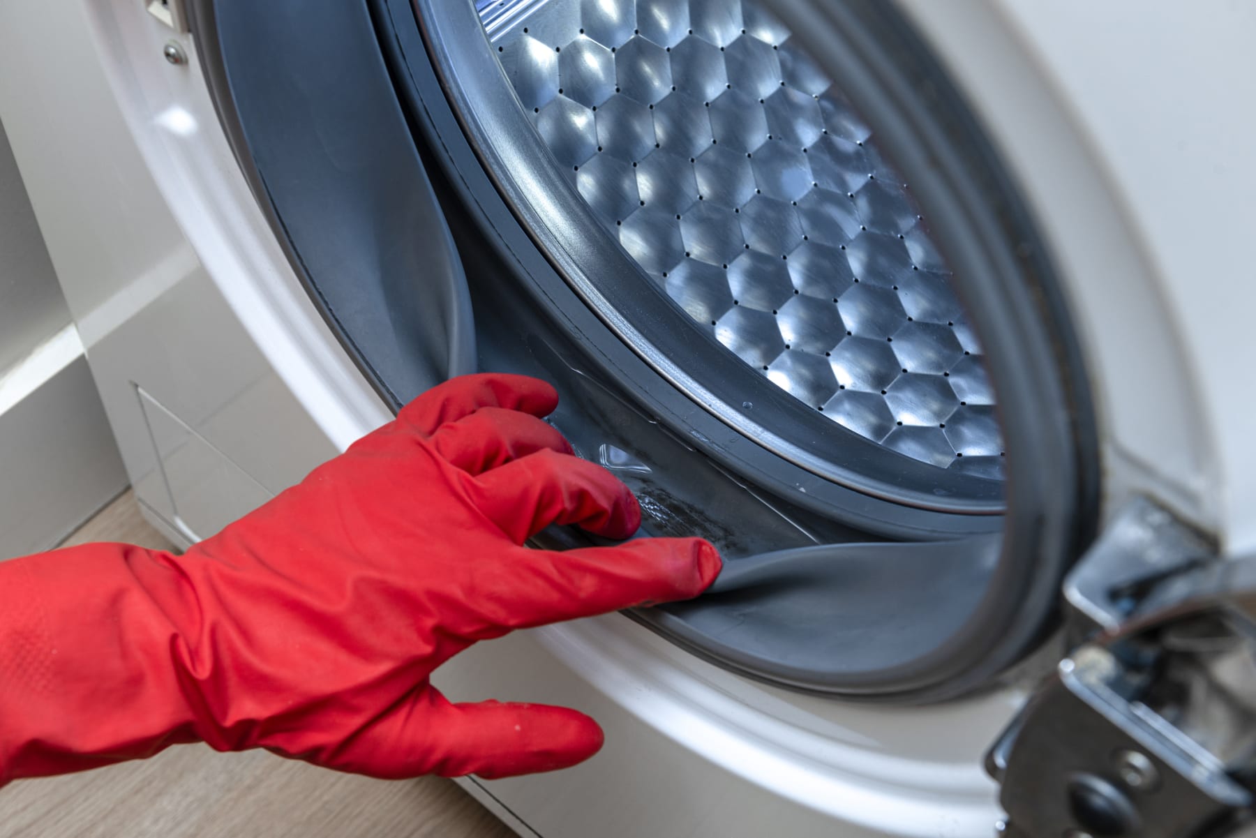 A gloved hand inspects a washer's rubber gasket