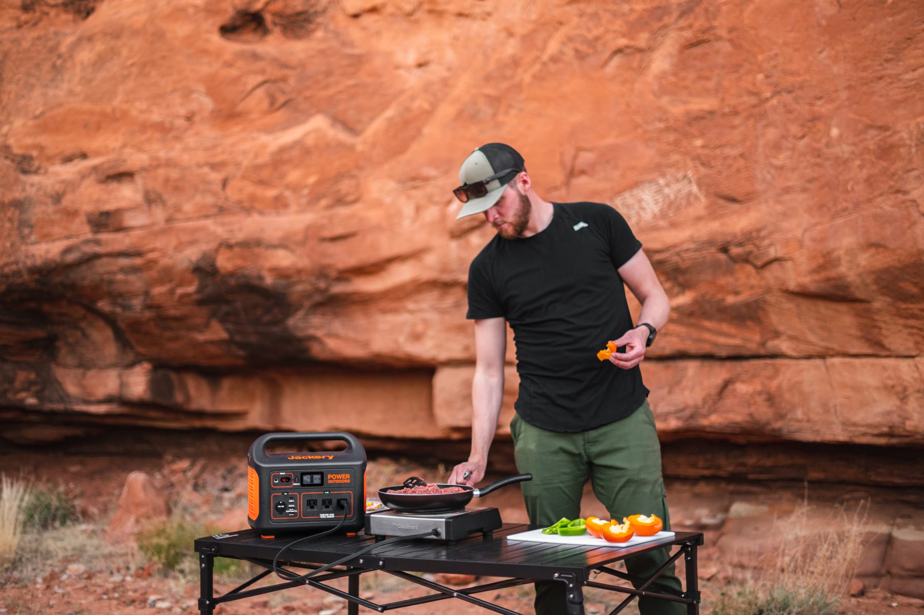 A man cooking outdoors using a hotplate and portable power station.