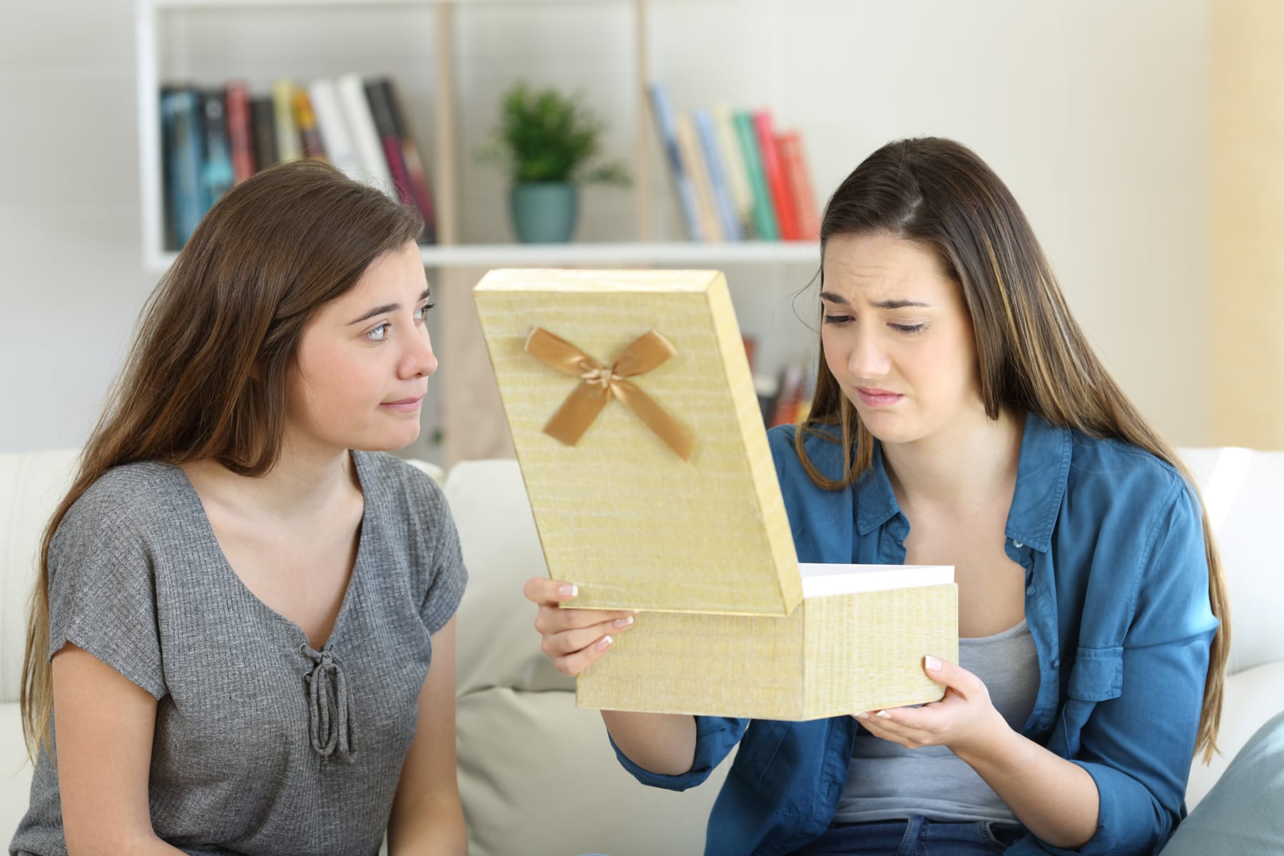 Two women open a gift and look displeased.