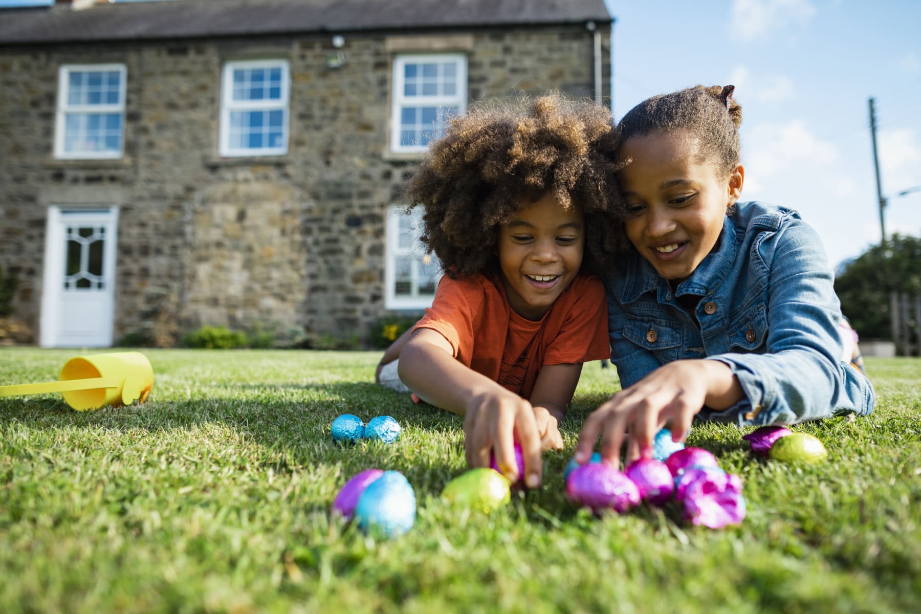 Siblings play with Easter eggs on lawn.