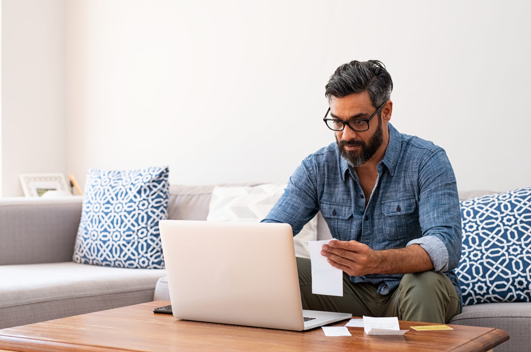 Man holds paper while using laptop.