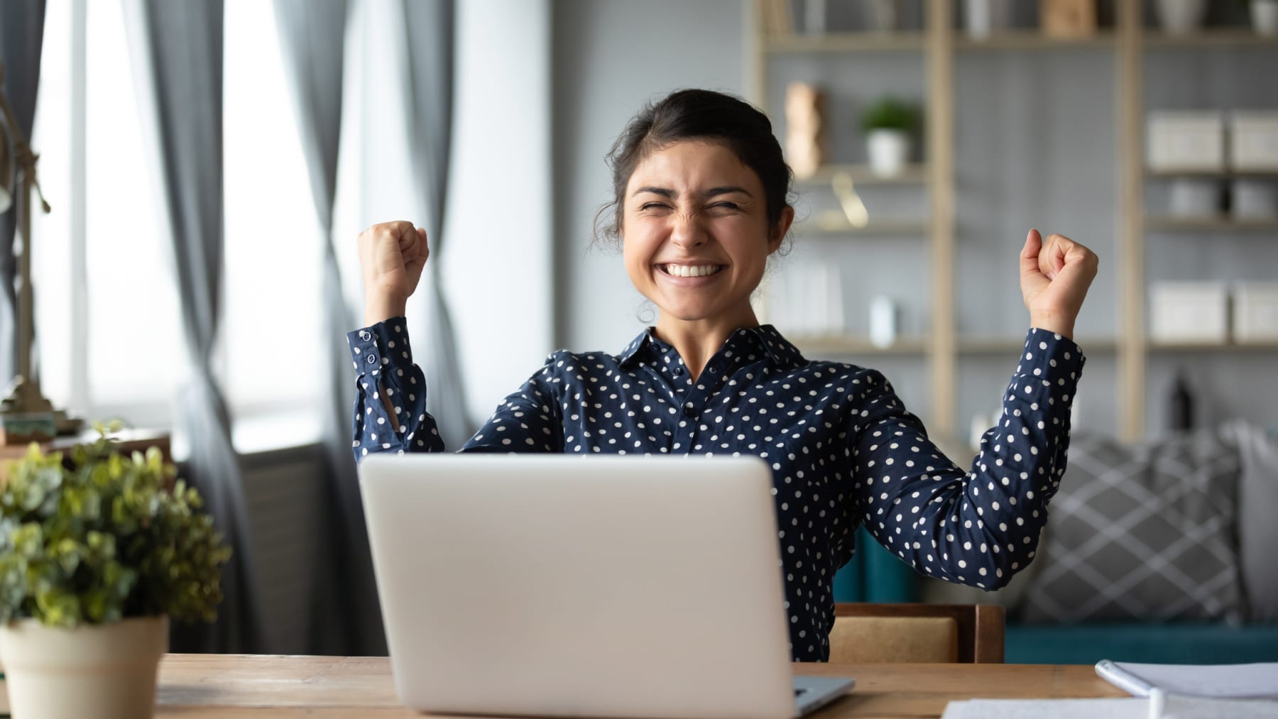 Young woman celebrates in front of laptop.