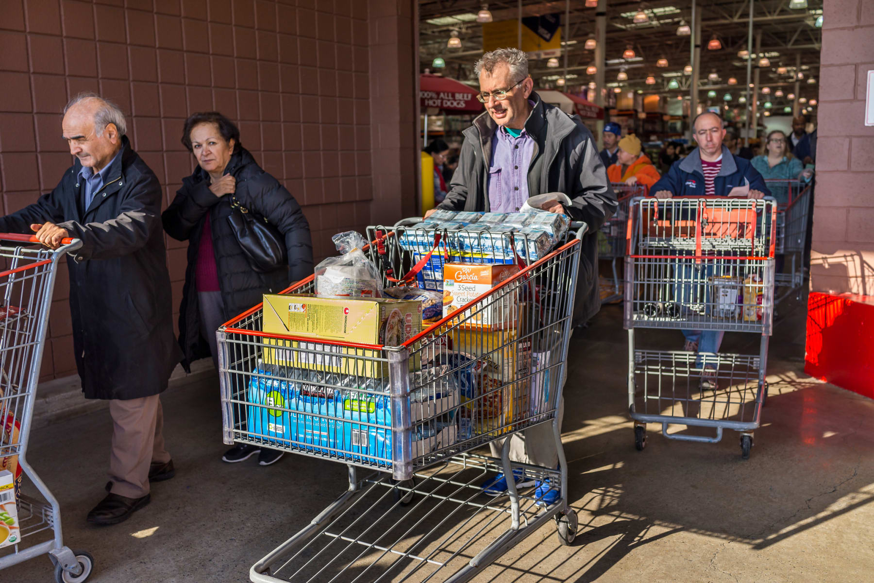 People with shopping carts walk out of Costco store.