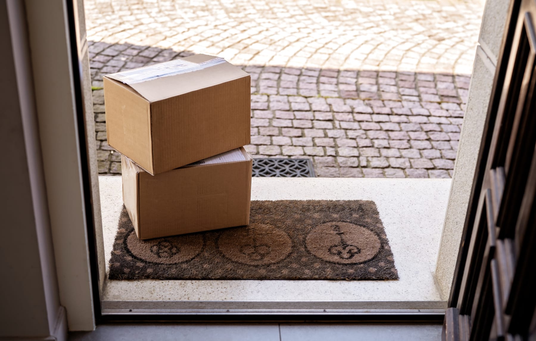 Two packages sit on mat outside open door.