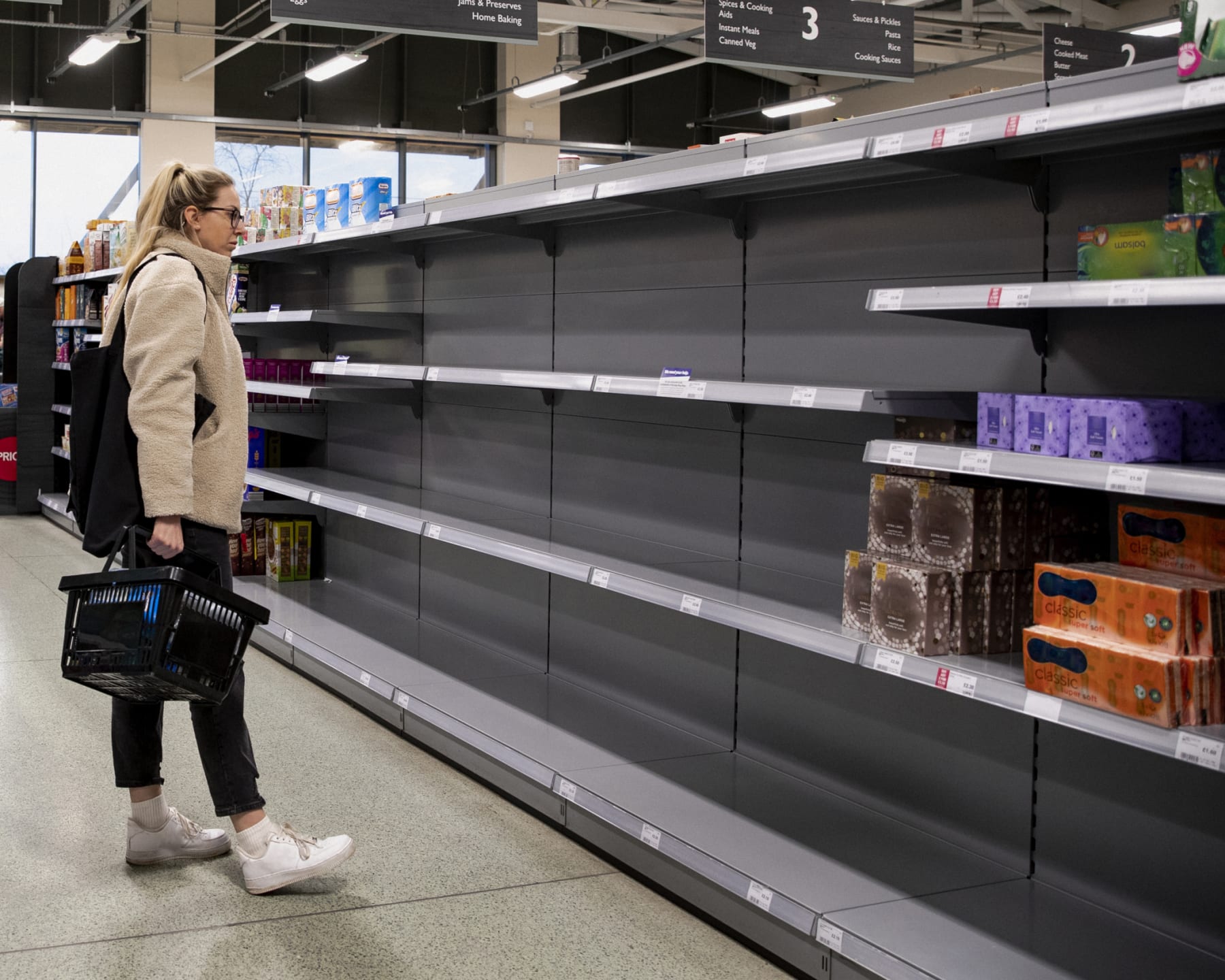 Woman looks at empty shelves in grocery store.