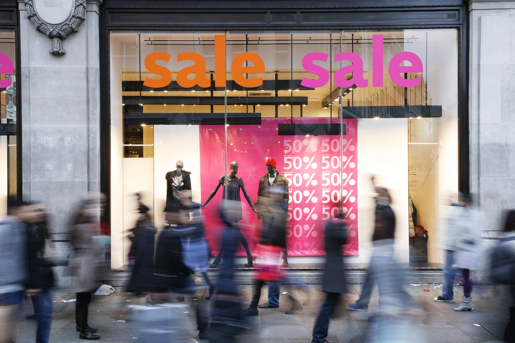 People walk by store window advertising a sale.