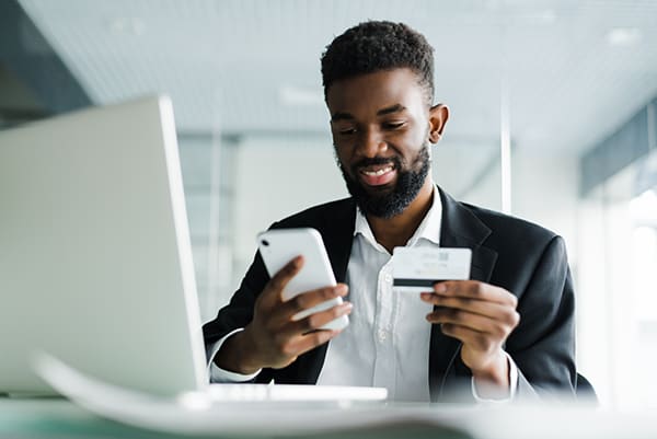 Man paying with a credit card online while holding his mobile phone and laptop